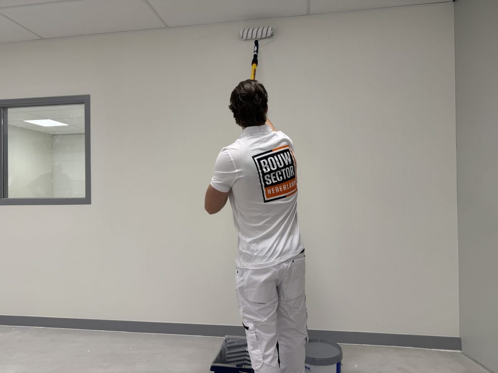 Schilder rolt de bovenkant van een lichte wand in een lege ruimte met een betonvloer