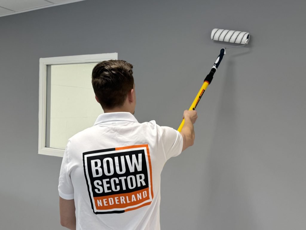 Schilder met het Bouwsector Nederland-logo op zijn rug zet een grijze muur naast een binnenraam met de roller