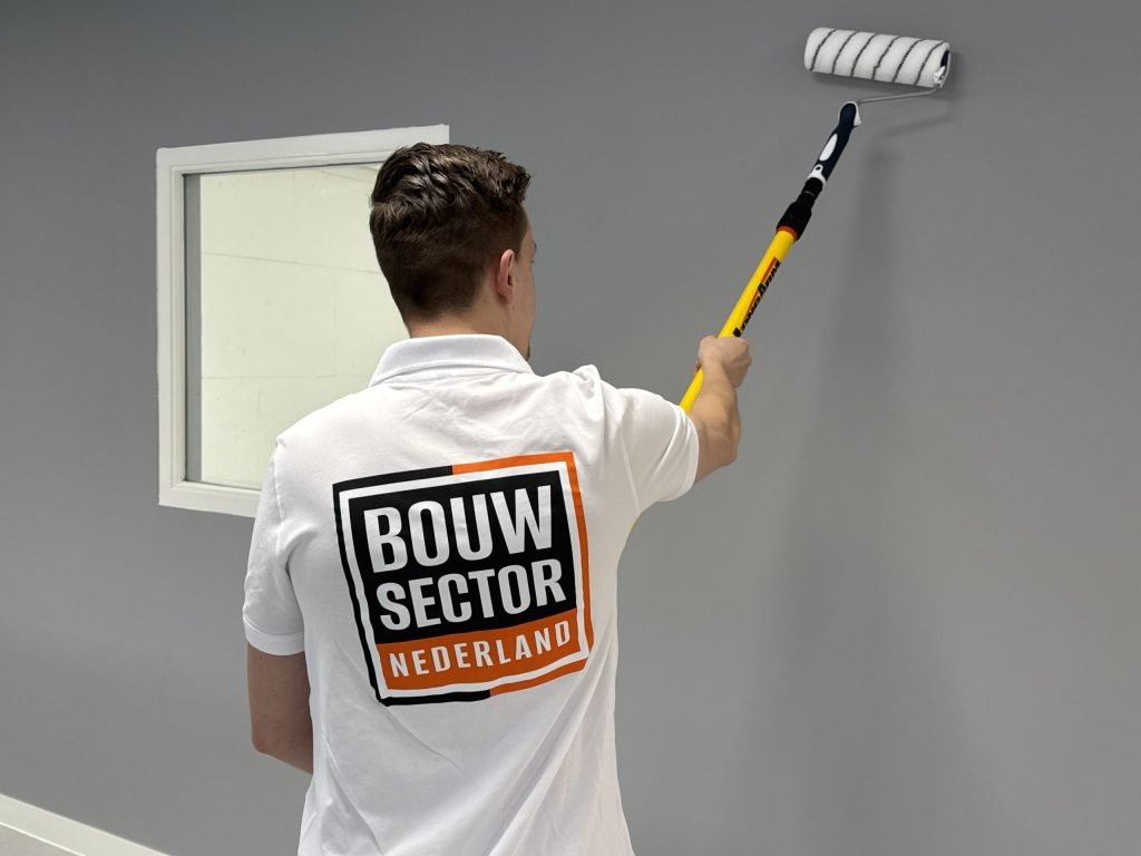 Schilder van Bouwsector Nederland rolt de bovenrand van een grijze wand bij een binnenraam